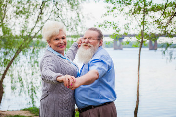 Elderly couple in love dancing on the background of the river in the park