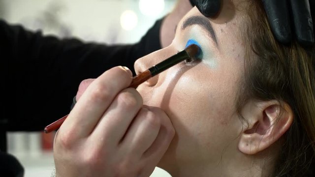 Man makeup artist making the face art with blue shadows closeup