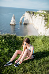 Young woman in sportswear tying shoelaces sitting outdoors on the beautiful rocky coastline background near Etretat town in France