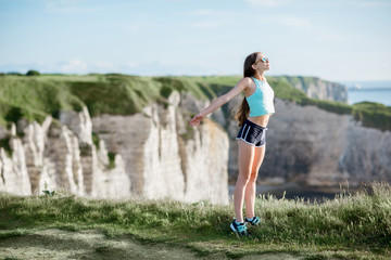 Young woman in sportswear breething deeply after the training standing on the beautiful rocky coastline background near Etretat town in France