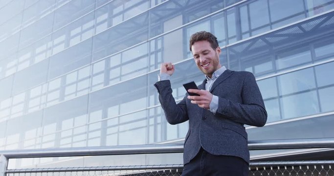 Success and achievement - happy businessman cheering celebrating looking at cell phone. Young urban professional successful business man receiving good news in business. Smartphone app concept