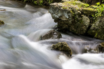 Long exposure of river in the forest with a mossy rocks