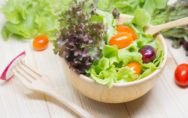 Salad in a wooden bowl on a wooden table, lettuce, tomatoes, cherries.