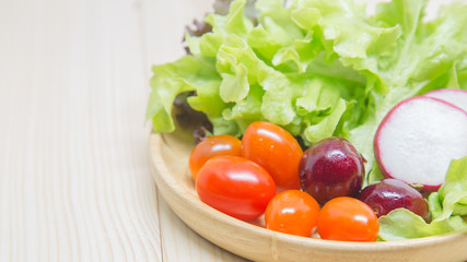 Salad in a wooden bowl on a wooden table, lettuce, tomatoes, cherries.