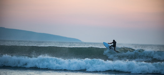 Surfer catching a wave at sunset - obrazy, fototapety, plakaty
