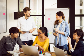 Multiethnic diverse group of creative team, casual business people in strategic meeting or project brainstorm discussion at office, using smartphone laptop and tablet. Startup or teamwork concept.