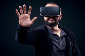 Young hipster bearded man wearing virtual reality goggles. Black background studio VR concept.