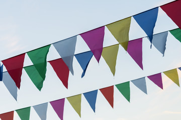 Garland of colorful flags of triangular shape, pennants against blue sky. City street holiday. Modern background, banner design. Fest, celebration concept
