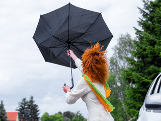 A woman stands next to a car and tries to clamp her umbrella
