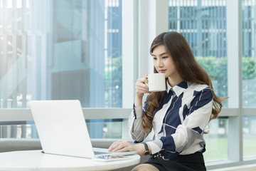 Cute asian woman drinking coffee at modern office workplace. Professional business woman relax from work.