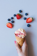 Hands holding ice-cream with berries on the blue background, top view
