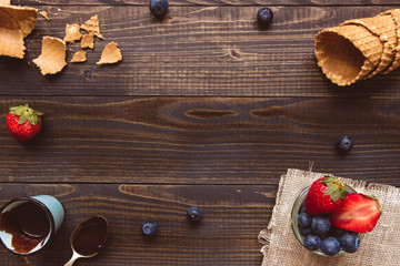 fresh berries, waffle cone and chocolate sauce on the wooden background, top view. Ice-cream background with copy space
