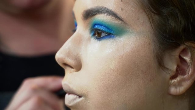 Makeup artist making the face art for brunette woman closeup