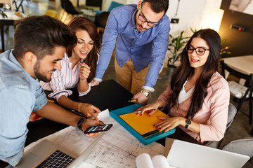 Group of casual architects and designers working on new project .They using laptop and discuss about blueprints.