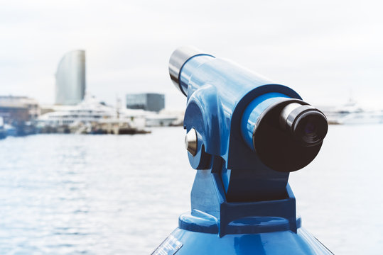 Touristic telescope look at city and sea with sunset view of Barcelona Spain, close up old blue binoculars on background viewpoint the pier port yacht, coin operated in panorama observation sunrise