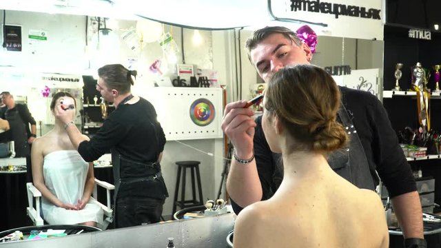 Makeup artist making beautiful face art for a young woman in front of the mirror