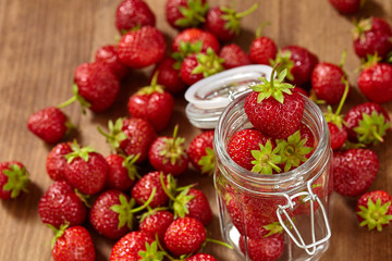 Fresh red strawberries for jam in a glass jar on the brown wooden table.