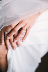 Bride's morning. young beautiful bride in white wedding dress and veil puting hand together on a knee. engagement ring with big diamond. wedding nail concept.