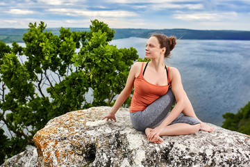 Beautiful young woman meditating in yoga pose at a big river against dramatic sky.