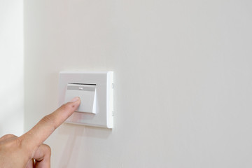 Men's fingers are extended to open the light switch on the wall.