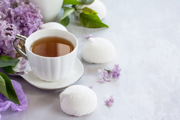 Delicate vanilla marshmallow on a white delicate plate. Still life with marshmallows, a cup of tea and lilac lilac against a vintage stone background. Copy space.
