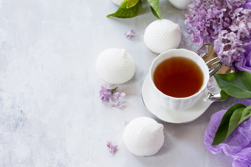 Delicate vanilla marshmallow on a white delicate plate. Still life with marshmallows, a cup of tea and lilac lilac against a vintage stone background. Copy space.