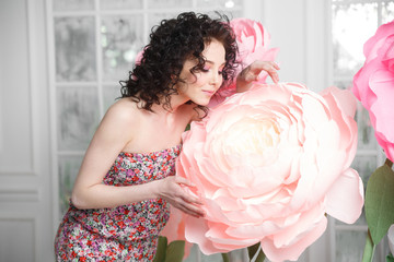 A beautiful slender brunette girl holds a huge peony flower from the paper.