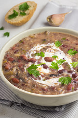 Spicy black bean soup in a white bowl on a concrete background. 