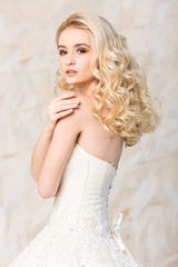 Fototapeta na wymiar fashionable gown, beautiful blonde model, bride hairstyle and makeup concept - young romantic lady in white wedding dress, slender woman stand indoors on light background, side view on hands and back