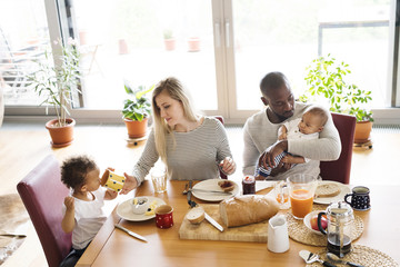 Young interracial family with little children having breakfast.