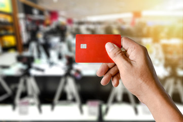 a hand holding credit card on blurred camera shop store
