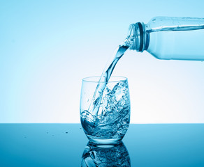 Bottle with creative splashing water in the glass on blue background.