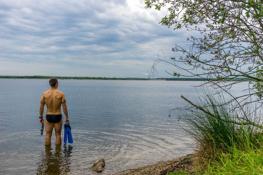 Mann mit Schwimmbrille und Flossen am See, Training für einen Triathlon 