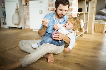 Young father at home feeding his little son with yoghurt.