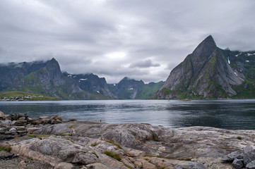 Fototapeta na wymiar Spiky rocky mountains in the clouds towering over the lake (Lofoten, Norway)