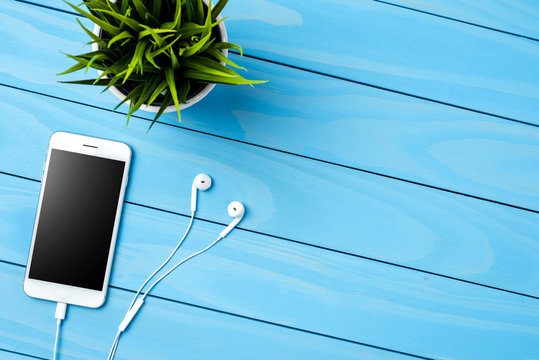 White Smart Phone And Green Plant On Blue Wooden Table