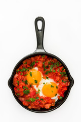 Shakshuka in iron frying pan isolated on white background. Typical food in Israel.
