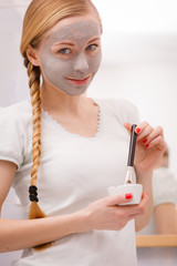 Woman applying with brush clay mud mask to her face