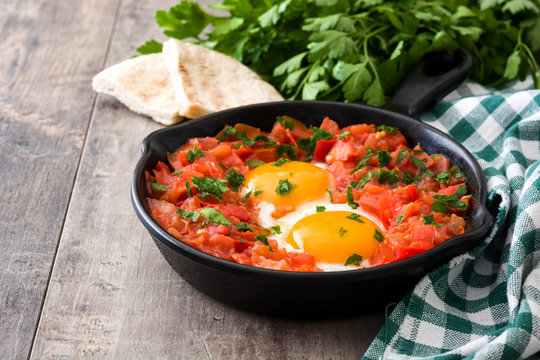 Shakshuka in iron frying pan on wooden table. Typical food in Israel.
