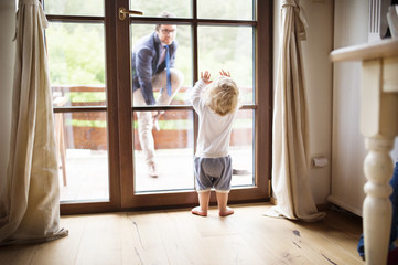 Businessman coming home, little son at the door welcoming him.