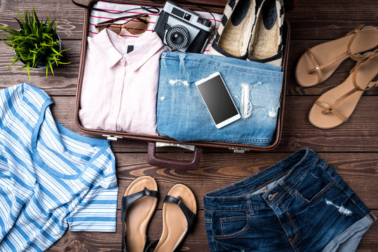 Open Suitcase With Casual Female Clothes On Wooden Table