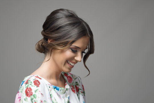 Portrait Of Shy Timid Smiling Beautiful Woman Looking Down Expression Over Gray Studio Background.