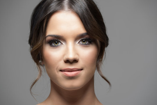 Close up horizontal portrait of young beautiful woman face smiling at camera with copyspace over gray studio background.