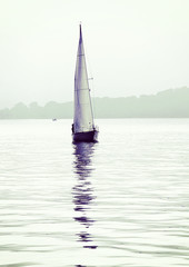 solitary sailboat with  reflection on sea calm waters