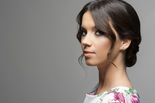 Gorgeous hispanic beauty woman with bun hairstyle and smoke eyes looking at camera over gray studio background.