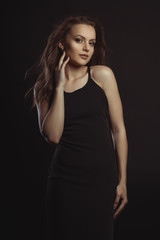 Fototapeta premium Pretty brunette model in black dress posing at studio