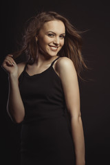 Naklejka premium Smiling brunette model in black dress with curly hair in motion