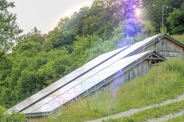 solar panels mounted on green hill slope shoot on sunset. lens flare