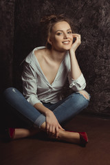 Happy young model in shirt and jeans sitting on the floor