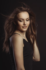 Naklejka premium Smiling brunette model in black dress with curly hair in motion